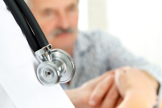 Doctor holding eldery patient's hand carefully - focus on stethoscope.