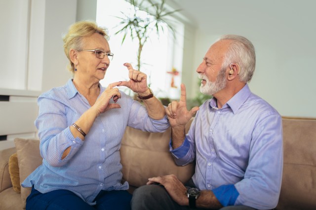 Smiling senior woman talking using sign language with her hearing impairment man