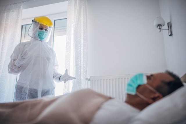Female doctor talking to senior man who is lying in bed infected with coronavirus