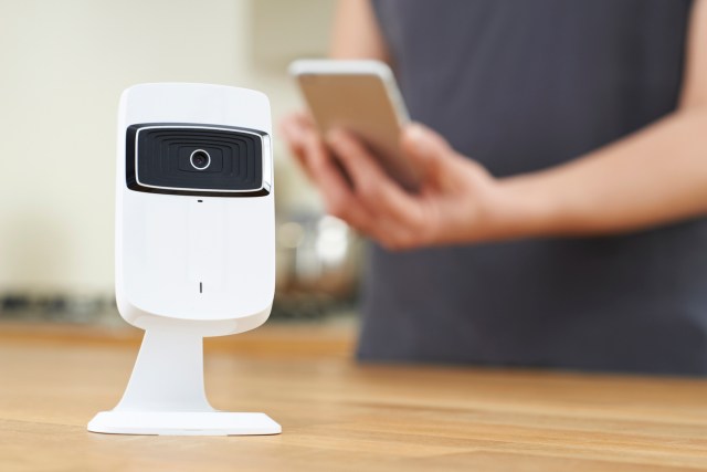 Woman Controlling Smart Security Camera Using App On Mobile Phone