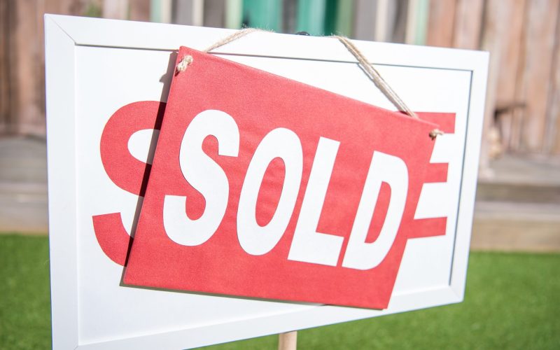 sale banner with sold card standing near new house