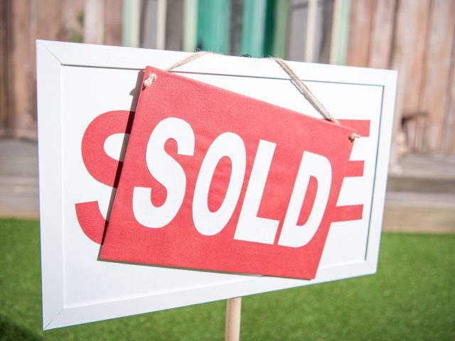 sale banner with sold card standing near new house