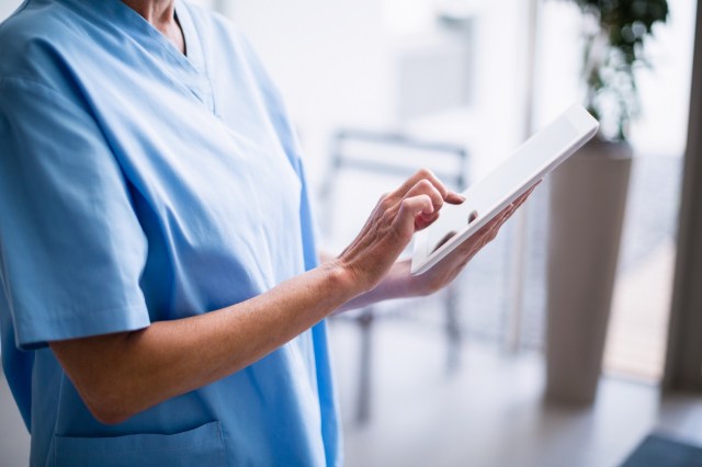 Nurse standing in hospital corridor using digital tablet