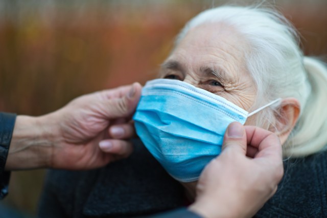 Man's hands helping a senior woman to put on protective face mask outdoors during COVID-19 pandemic