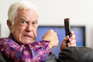 Furious senior man with TV remote control shakes fist