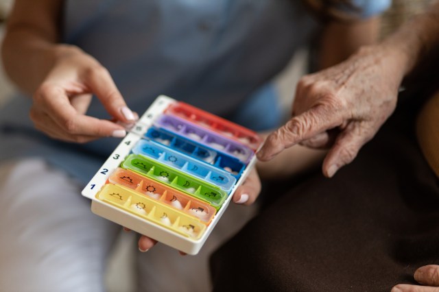 Nurse home health care visit holding weekly pill box for senior woman