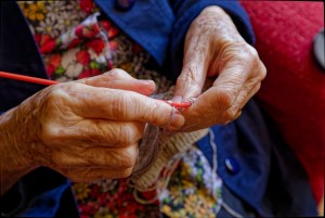The wrinkled hands of a 88 year old grandmother busy knitting a woolen article.