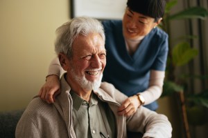 Portrait of a Smiling Elderly Man Taking a Jacket off With a Help of a Woman in a Care Home