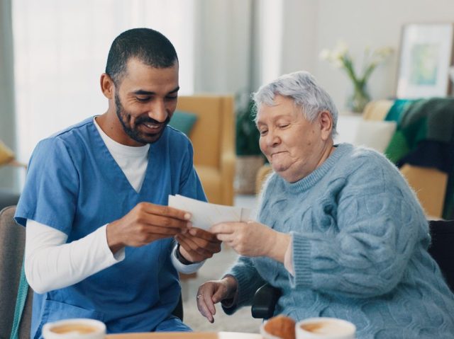 Nursing home, photo album and caregiver with old woman in retirement, break and bonding together. Love, memory or senior person with pictures for support or nostalgia with care, nurse or conversation