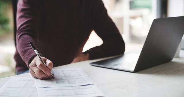 Hands, laptop and finance with a business man writing on documents at a desk in his office at work. Accounting, computer and contract with a male employee signing a document in the workplace