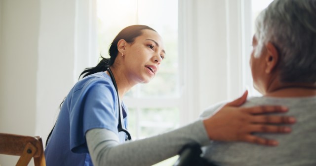 Woman, nurse and senior patient in wheelchair for elderly care, support or trust at old age home. Medical doctor or caregiver listening to person