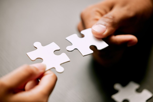 Closeup shot of two unrecognizable businesspeople holding puzzle pieces together