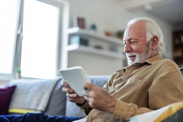 Portrait of happy senior man in office with tablet, email or social media for business, schedule or agenda. Smile, digital app and businessman networking online for market research, website and report.