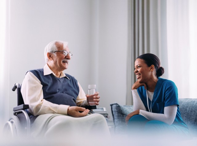 Elderly Man in Wheelchair Laughing with Caring Nurse at Home