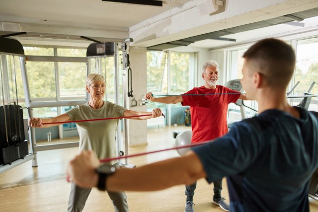 Senior couple exercising with personal trainer using resistance band