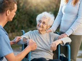 Support, caregiver and senior woman in wheelchair with help, medical healthcare and disability assistance from male nurse. Volunteer worker, adult daughter and disabled patient on nursing home estate