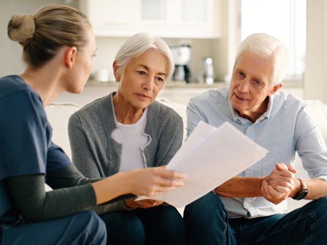 Senior couple, nurse and documents in life insurance, budget planning or advice on sofa at home. Woman caregiver or medical healthcare worker consulting elderly people on paperwork in retirement plan